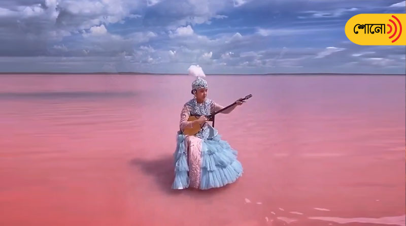 Woman plays music in the middle of a lake that has turned pink